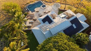 An aerial view of a modern house with a swimming pool, solar panels, and a patio area with lounge chairs.