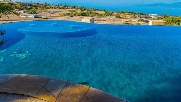 A clear blue infinity pool with a view of the ocean and distant mountains.
