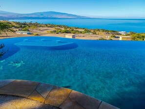 Ein klarer, blauer Infinity-Pool mit Blick auf das Meer und entfernte Berge.