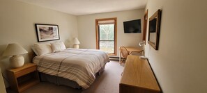 A bedroom with a bed, bedside tables, a desk, a chair, a TV, and a window.