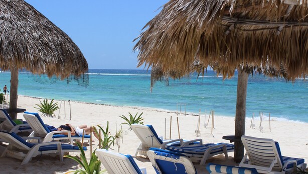 Une plage avec des chaises longues et des parasols en chaume.