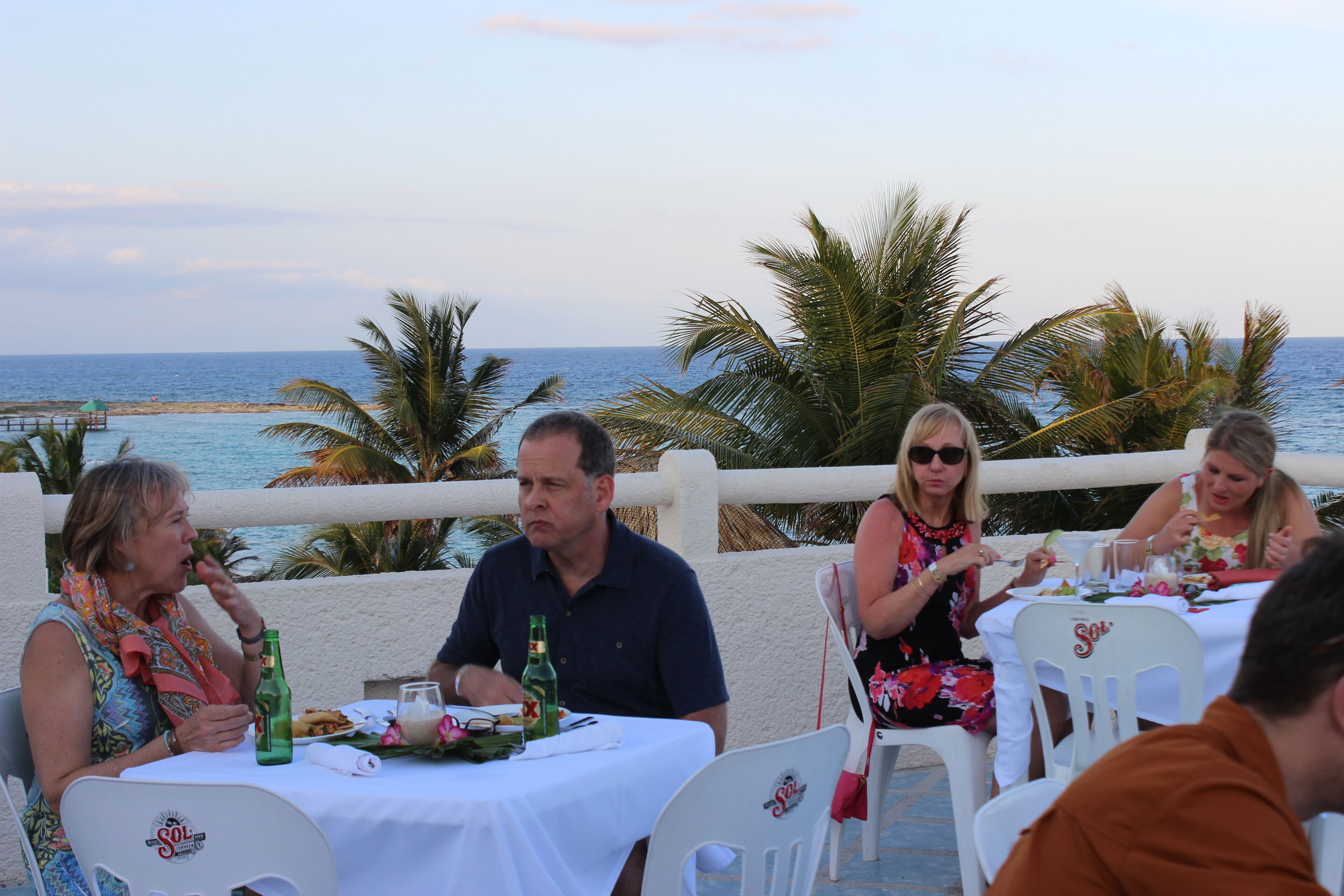 Un groupe de personnes est assis à une table en plein air, devant laquelle s’étend une vue sur l’océan.