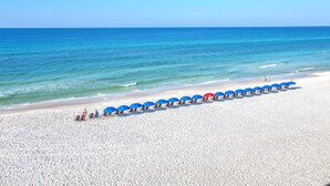 Une plage bordée de rangées de parasols bleus et rouges, avec du sable blanc et une eau d’un bleu cristallin.