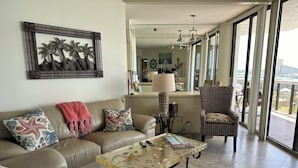 Un salon comprenant un canapé, un fauteuil et une table basse, une grande fenêtre offrant une belle vue et une œuvre d’art encadrée accrochée au mur.