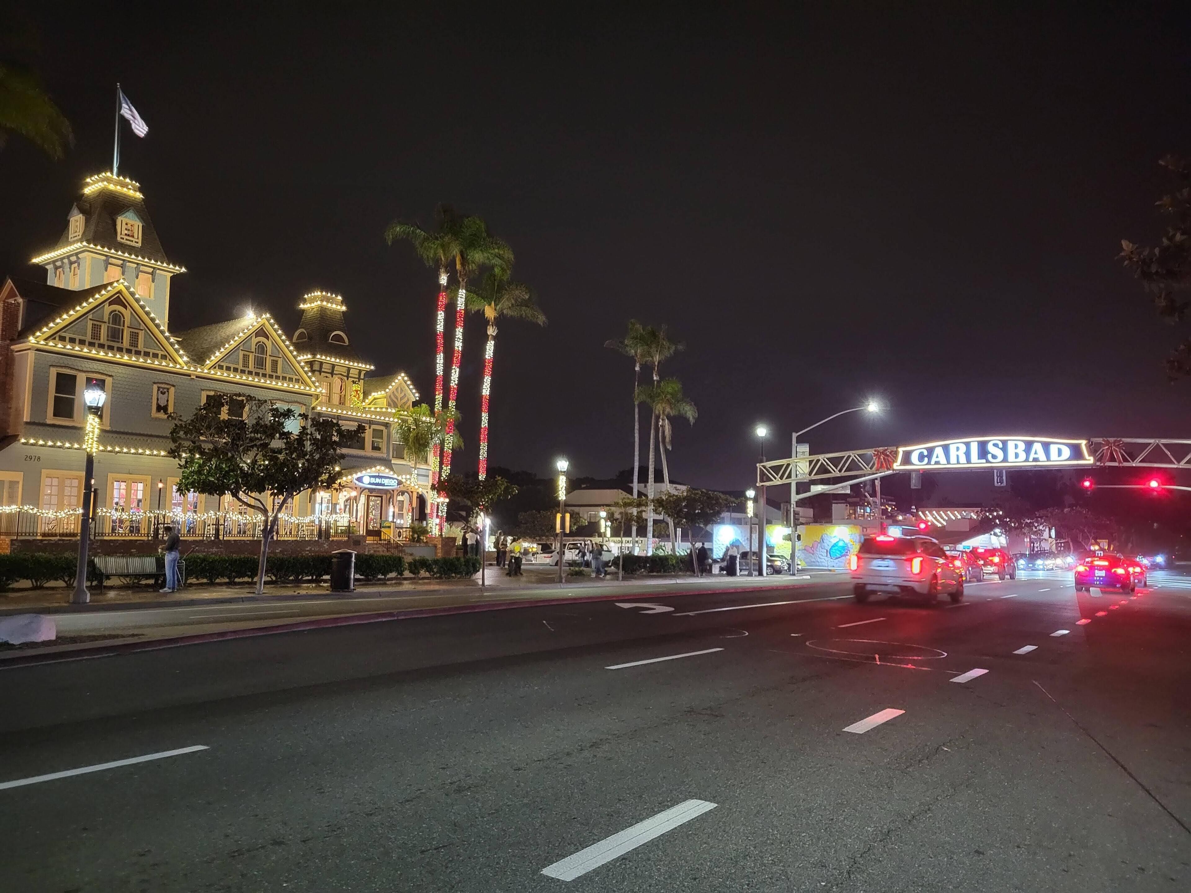A historic building with a clock tower, decorated with lights, and a sign reading "CARLSBAD" above a busy street.