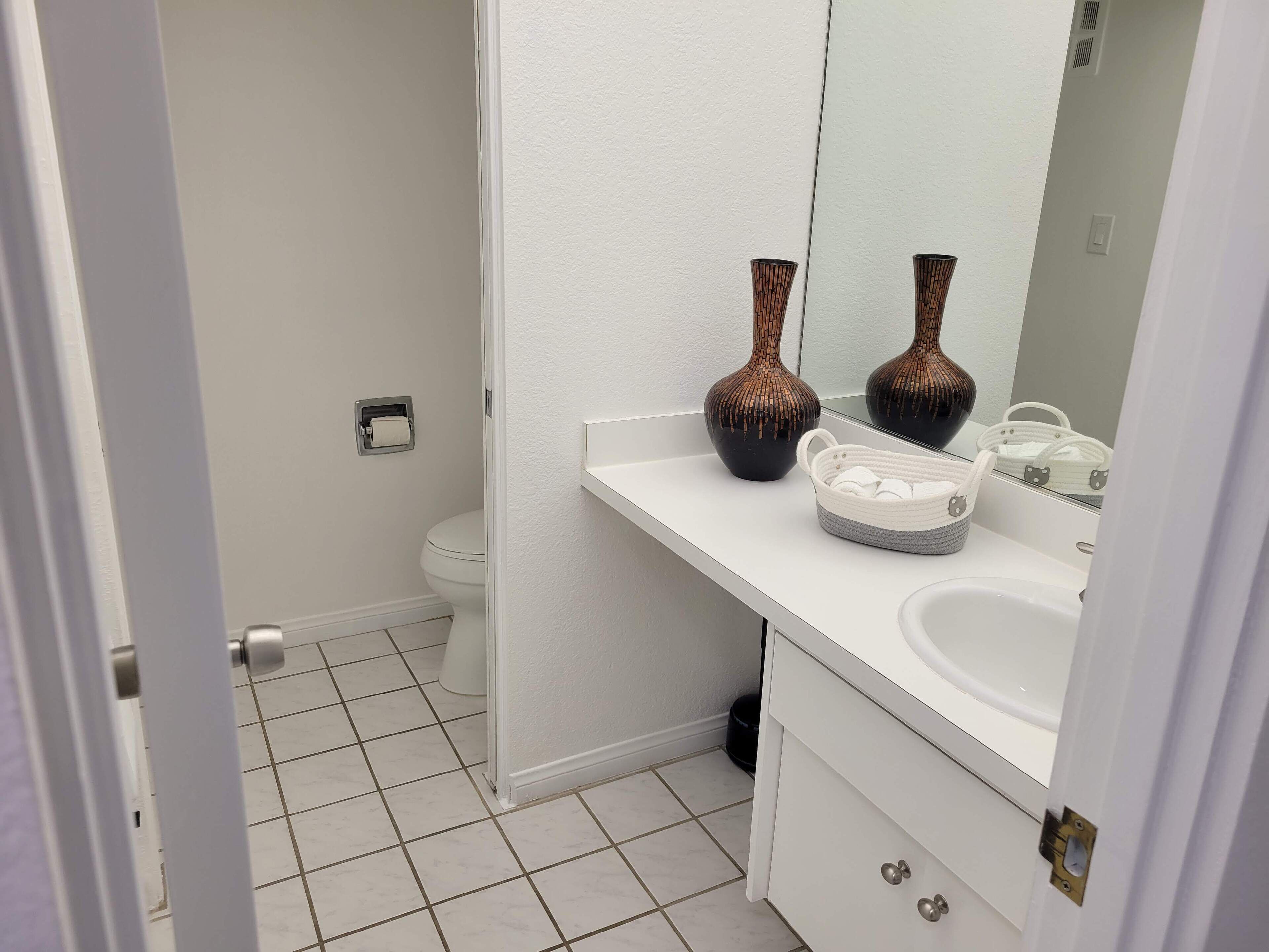 Une salle de bain avec un lavabo blanc, deux vases, un panier et des toilettes.
