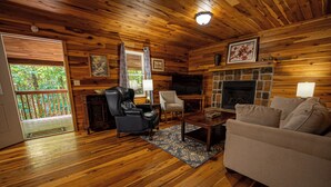 A cozy cabin interior with wooden floors, a fireplace, a television, and a comfortable seating area. - Mountaineer Cabin 6 - Hot Tub & Gas Fireplace close to New River Gorge (Hico)