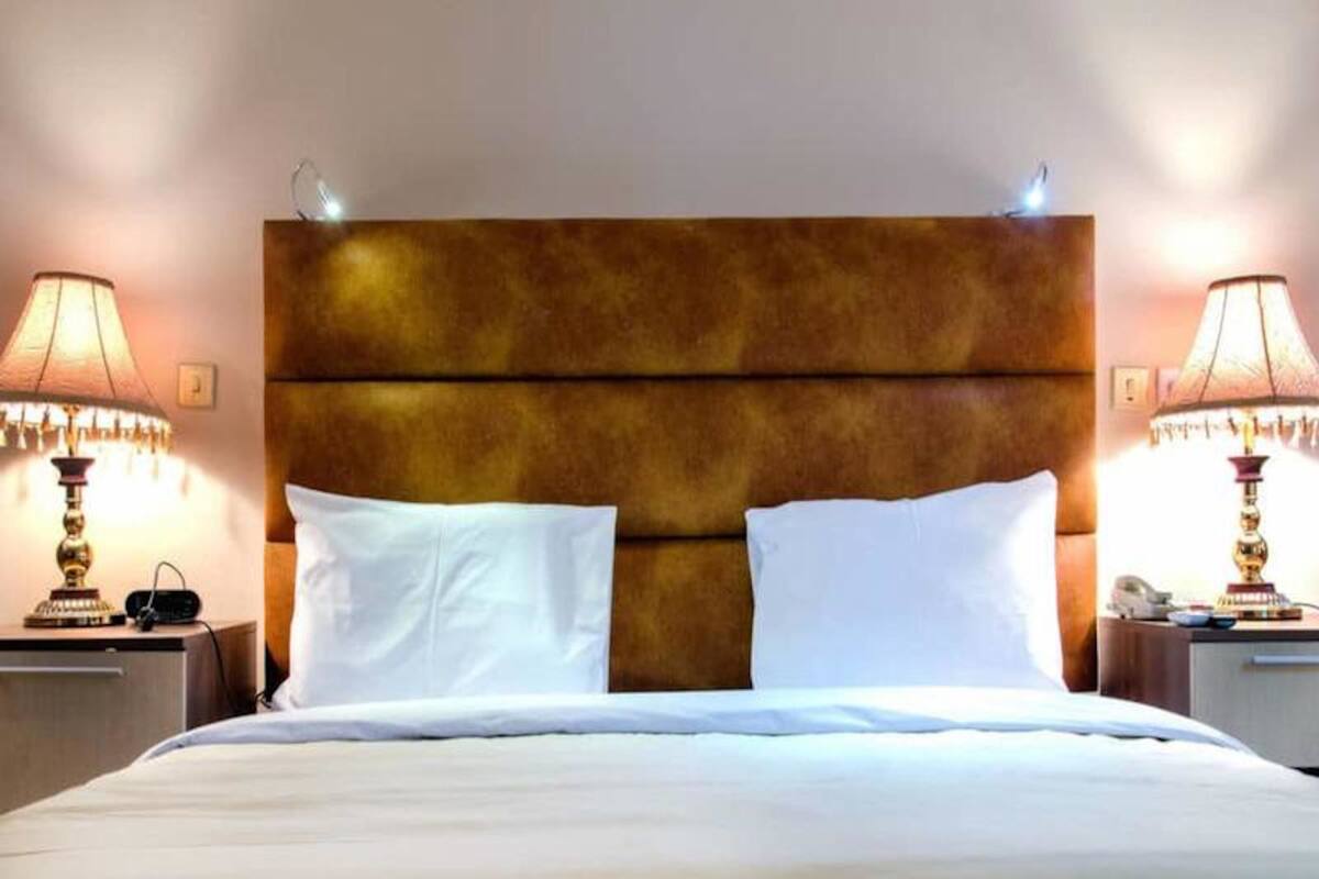 Quarto de hotel com uma cama grande, duas luminárias de cabeceira e uma mesa de cabeceira com telefone e abajur.