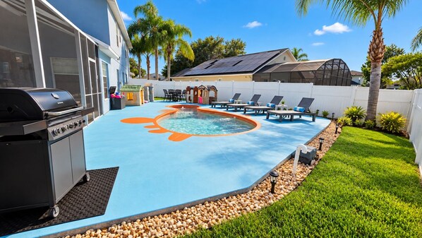 Un patio trasero con piscina, una parrilla y un área cercada con sillas de descanso.