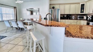 A modern kitchen with granite countertops, stainless steel appliances, and white cabinetry. There is a dining area with a table and chairs.
