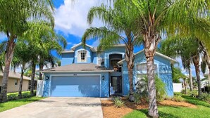 A blue two-story house with a garage, surrounded by palm trees and a well-maintained lawn.