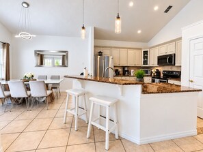 A modern kitchen with a central island, bar stools, and a dining area with a table and chairs. - 10 minutes to Disney! Two Pools & Spa! No Carpet! Themed Rooms @The Nemo House (Kissimmee)