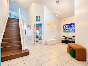 Un interior moderno con una escalera de madera, un letrero de neón, un cuadro colorido y una zona de estar acogedora.