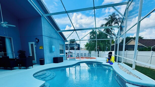 A swimming pool with a curved design, surrounded by a covered patio area with seating and a ceiling fan.