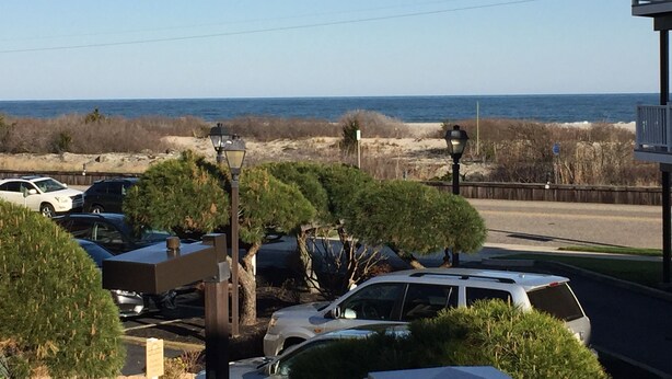 A parking area with several cars, a beach in the background, and a clear sky.