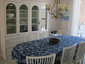 A dining area with a round table and white chairs, surrounded by a classic chandelier and a cabinet with glass doors.