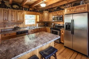 A kitchen with wooden cabinets, granite countertops, stainless steel appliances, and a large island with bar stools. - Luxury Lodge by Mountain Oasis | Luxury Views of North Georgia (Ellijay)