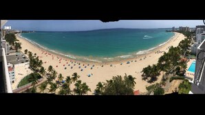 A beach with a clear view of the ocean, palm trees, and buildings in the background. - Marbella del Caribe Condo - Amazing Oceanfront View (Carolina)