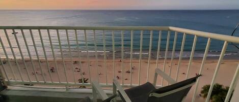 A balcony with a view of a beach and ocean during sunset.