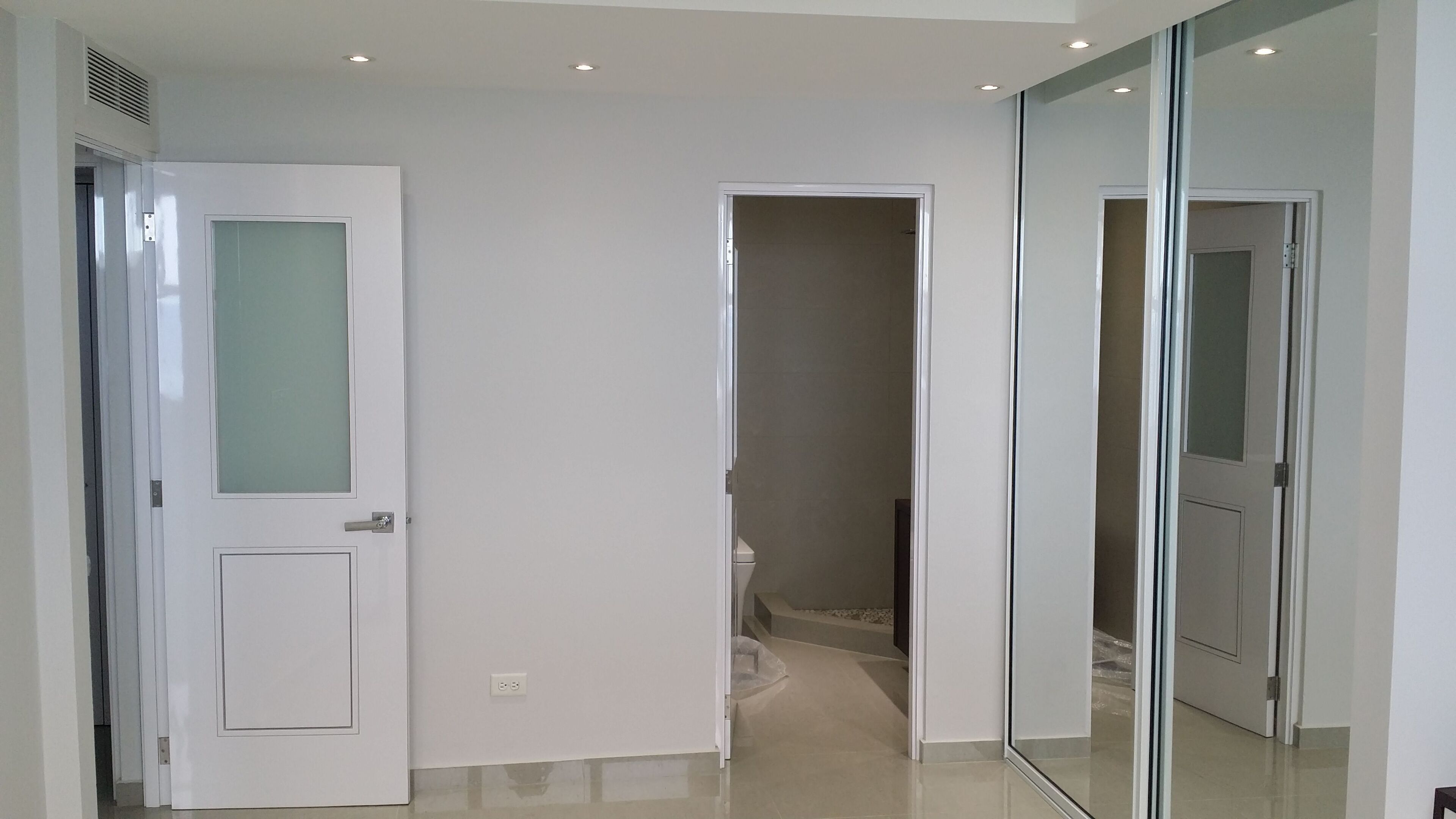 Un pasillo con paredes blancas, una puerta espejada y un piso de baldosas.