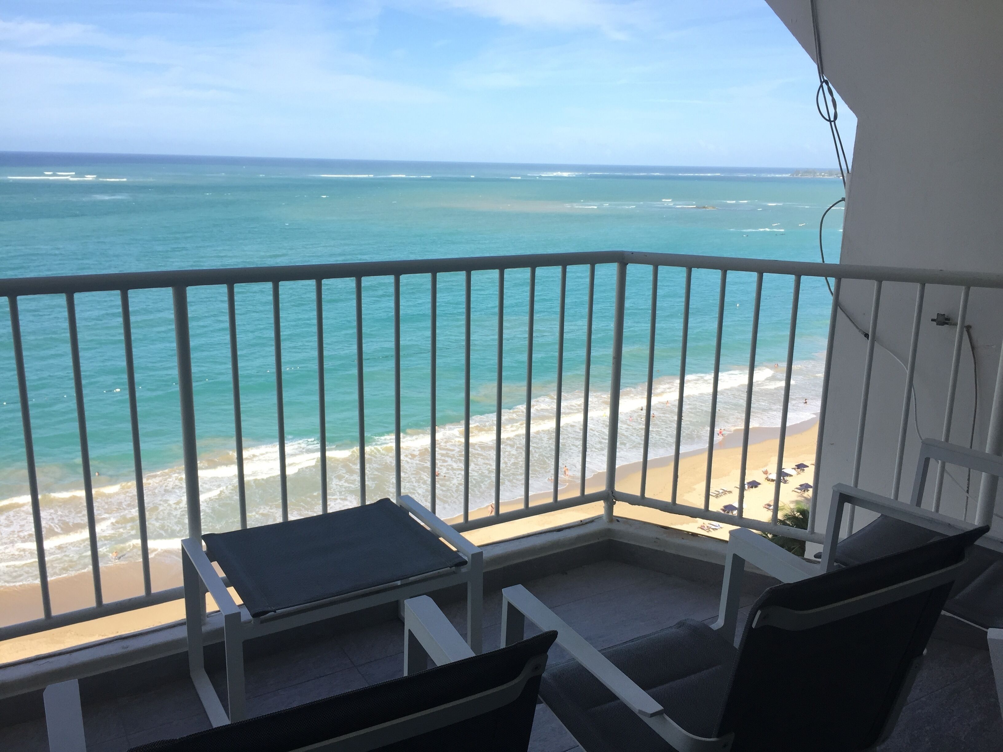 A balcony with a view of the ocean and beach. There are two chairs and a small table.