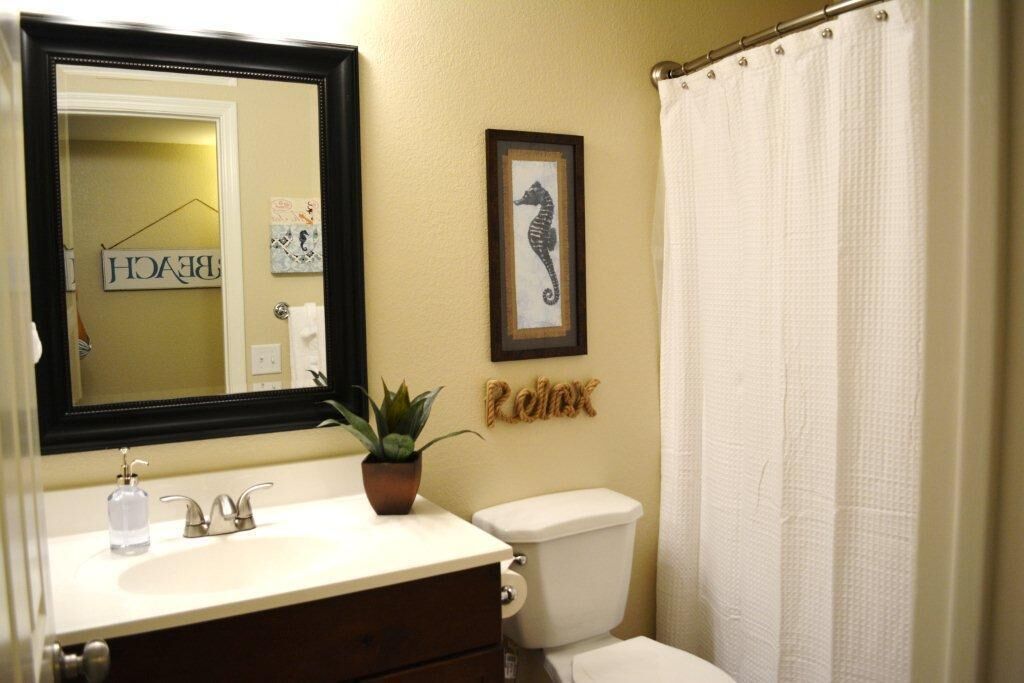 A bathroom with a white sink, a mirror, a framed seahorse picture, and a toilet.
