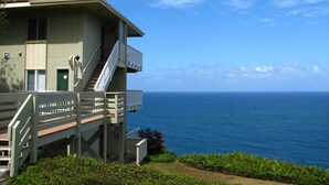A two-story building with a staircase leading to a balcony overlooking the ocean. - Gorgeous Ocean Views From All Rooms! Corner Unit! Cool AC! Aloha Galore! (Princeville)