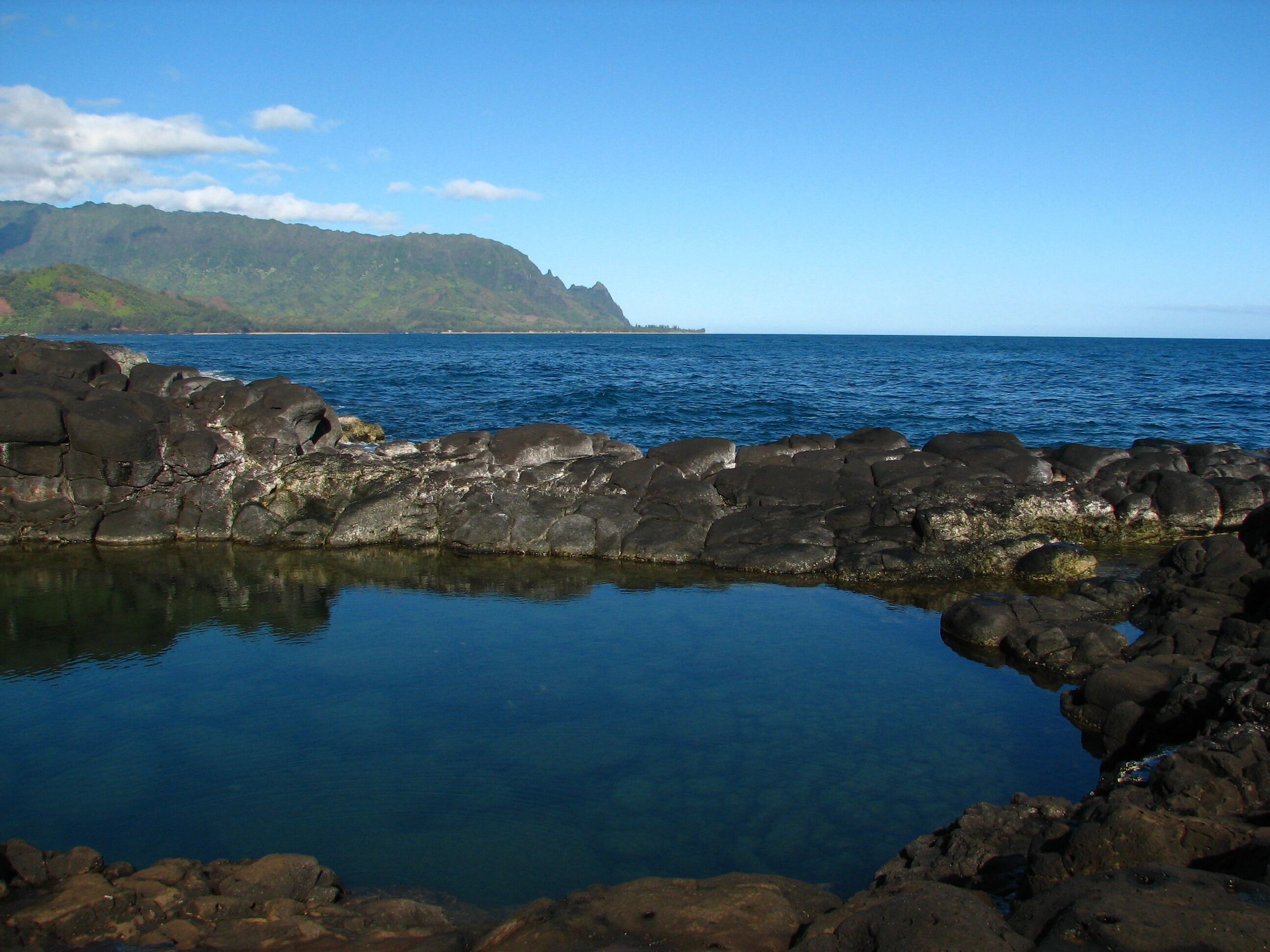 A rocky shoreline with clear blue water and a distant mountain.