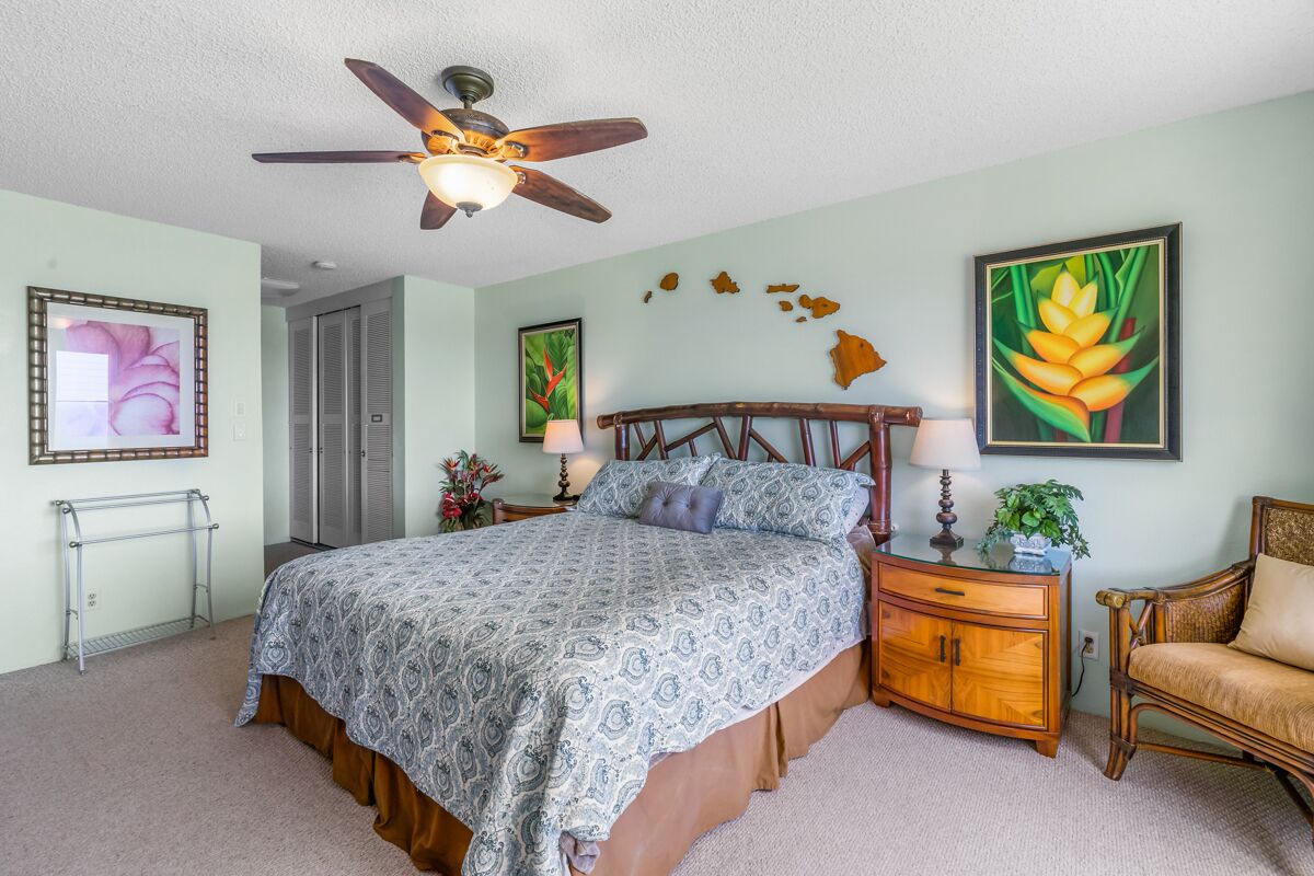 A bedroom with a bed, nightstands, a wooden dresser, a chair, a ceiling fan, and wall art.
