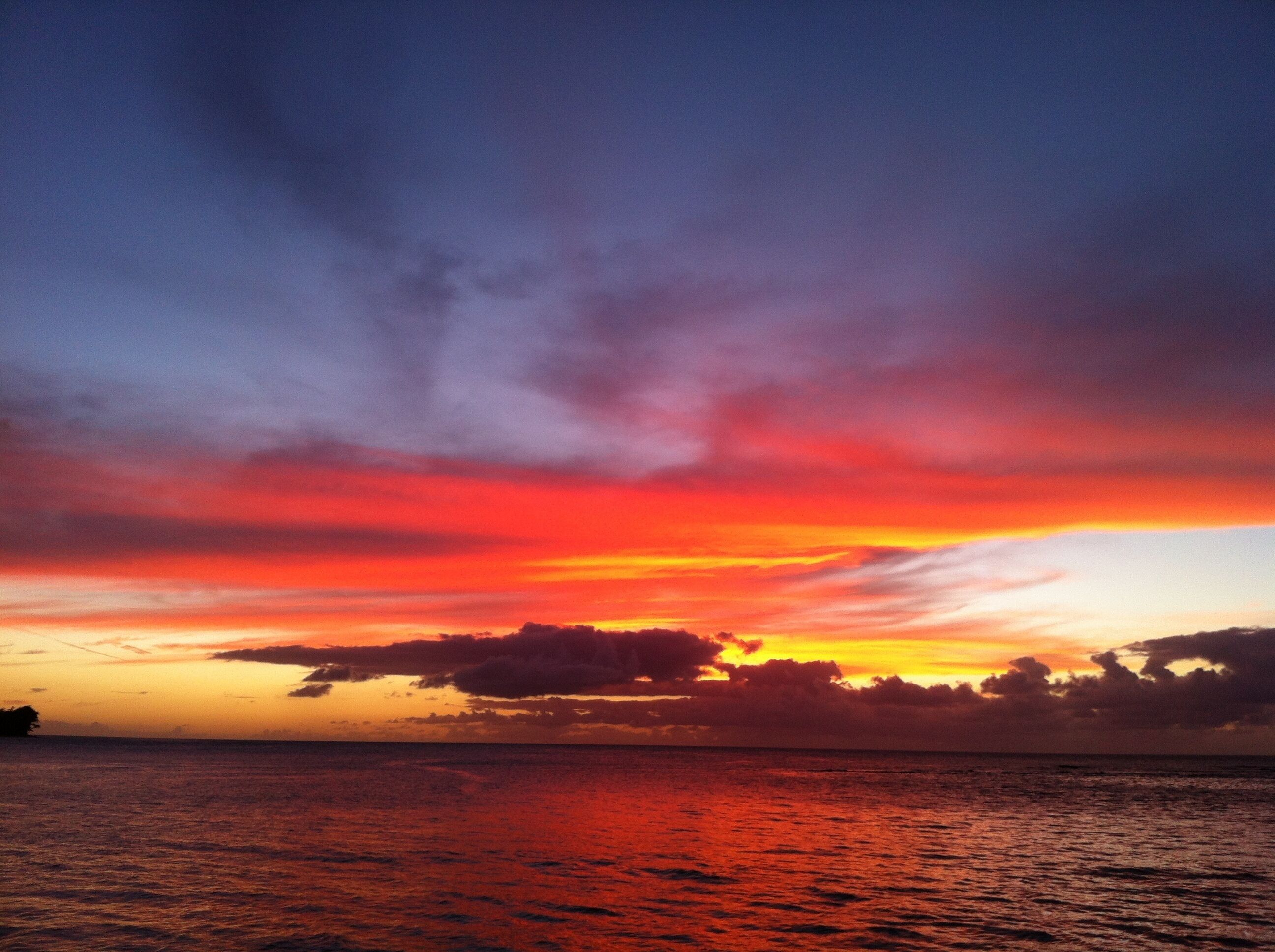 A sunset over the ocean with a clear sky and calm waters.