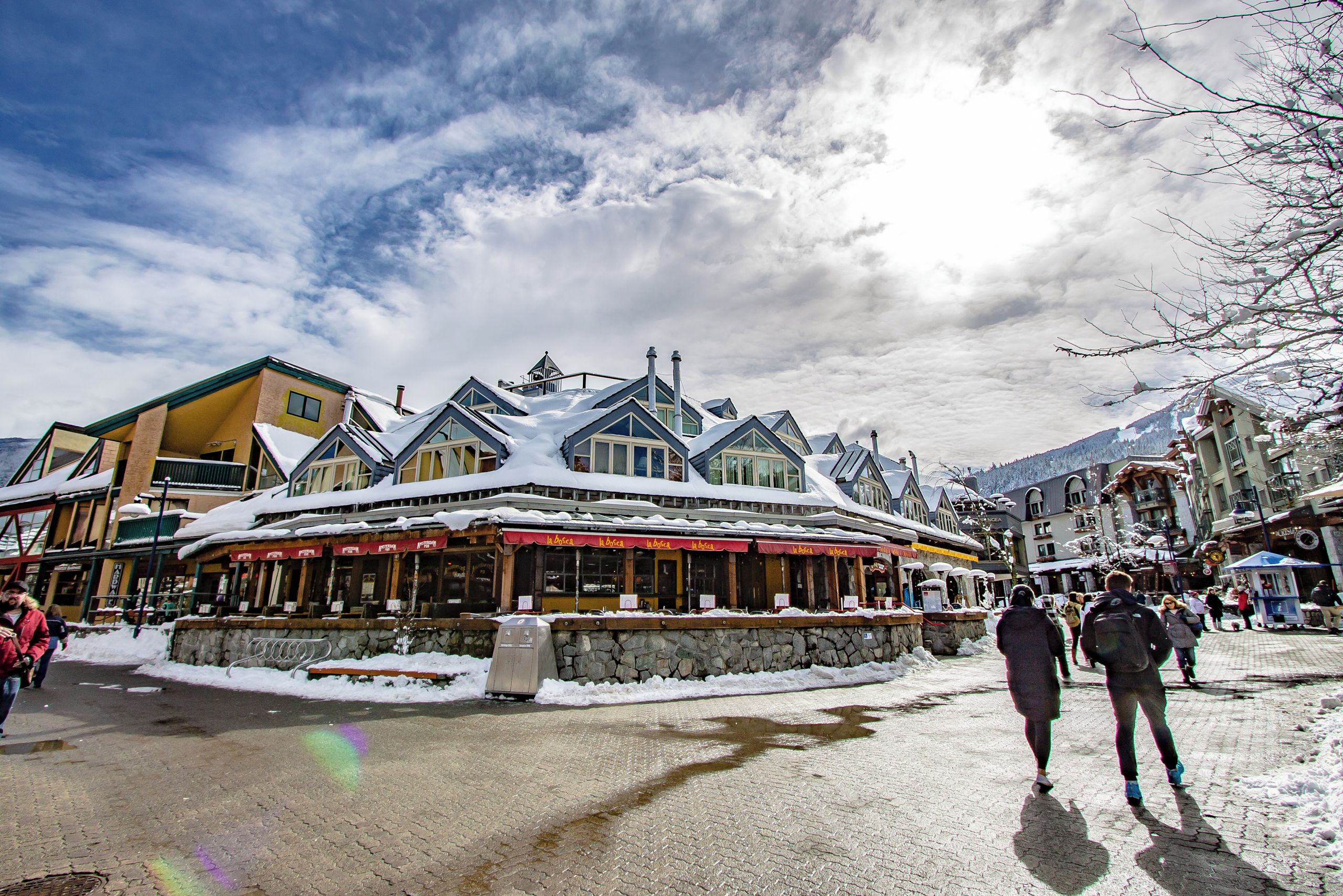 A snow-covered building with a stone base and wooden upper structure, featuring multiple windows and a red awning.