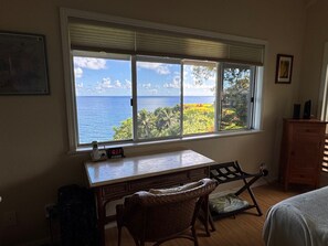 Une pièce dotée d’une grande fenêtre donnant sur un paysage magnifique, d’un bureau avec une chaise, d’une commode en bois et d’un tableau encadré accroché au mur.