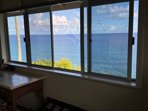 A room with a large window overlooking the sea, a wooden table, and a chair. - Kauai Oceanfront Condo Princeville, Pali Ke Kua 218, Best views, Corner unit (Princeville)