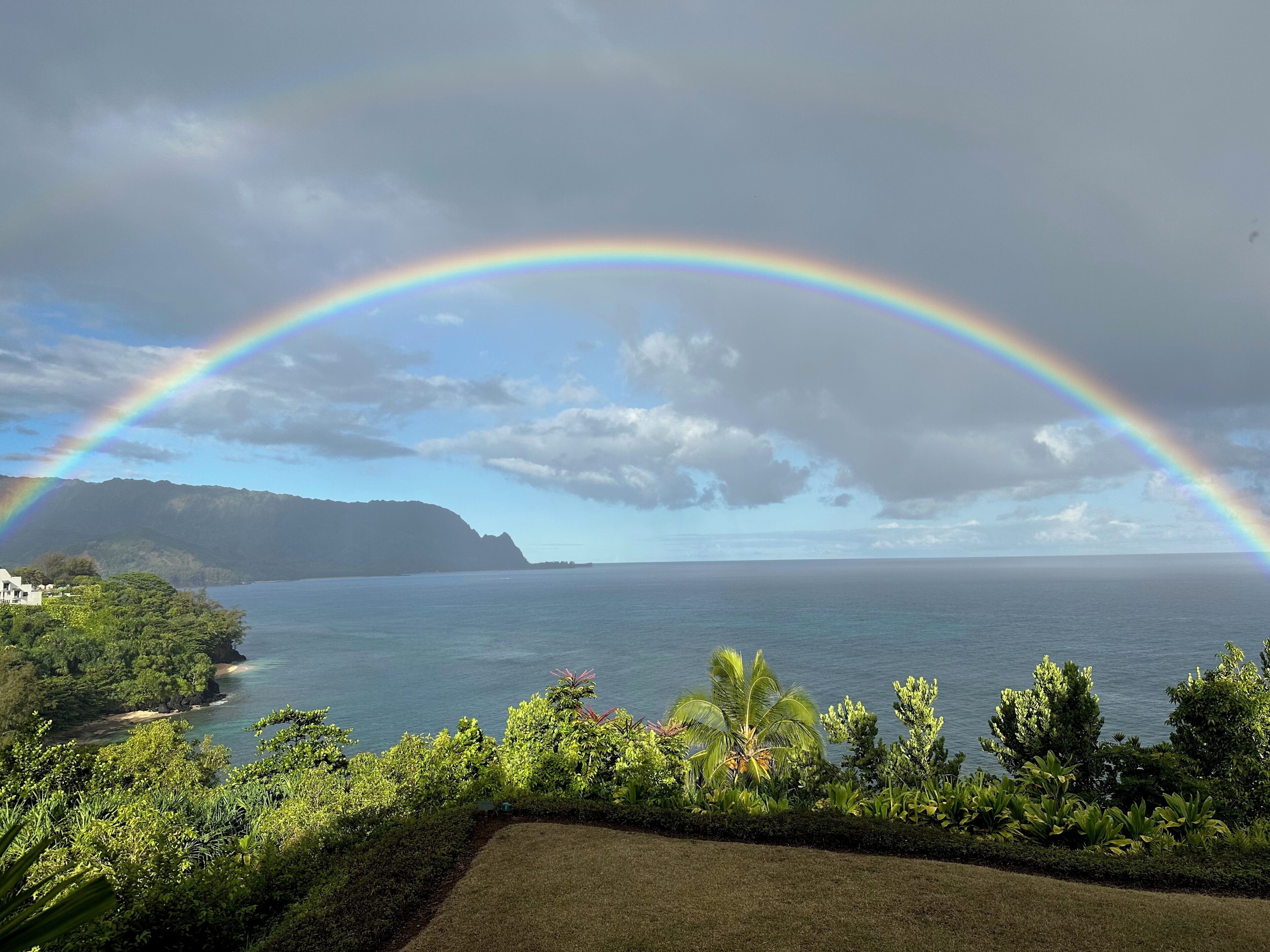 Een kustlandschap met een regenboog, begroeiing en uitzicht op zee.