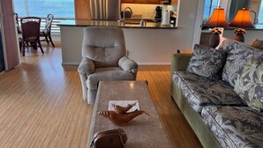 Una sala de estar con vista al océano, una cocina con armarios de madera y electrodomésticos de acero inoxidable, y un comedor con sillas de mimbre.