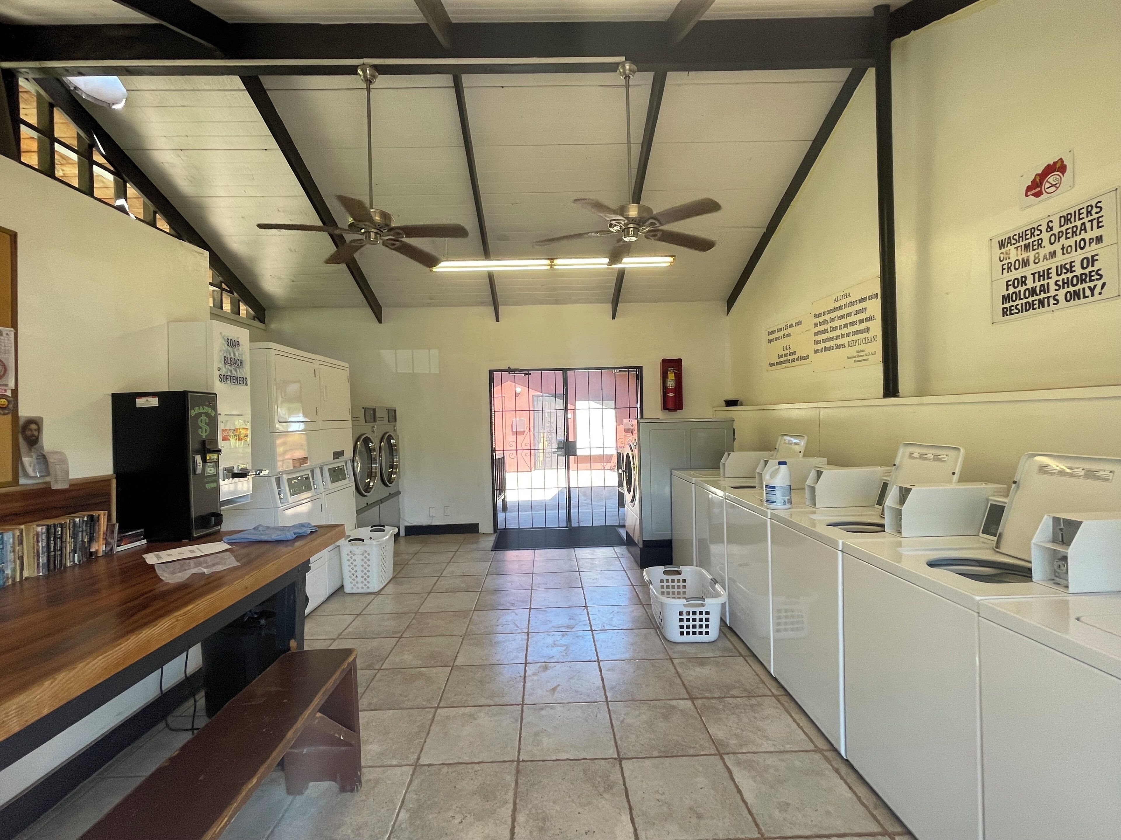 A laundry facility with ceiling fans, washing machines, dryers, and a refrigerator.