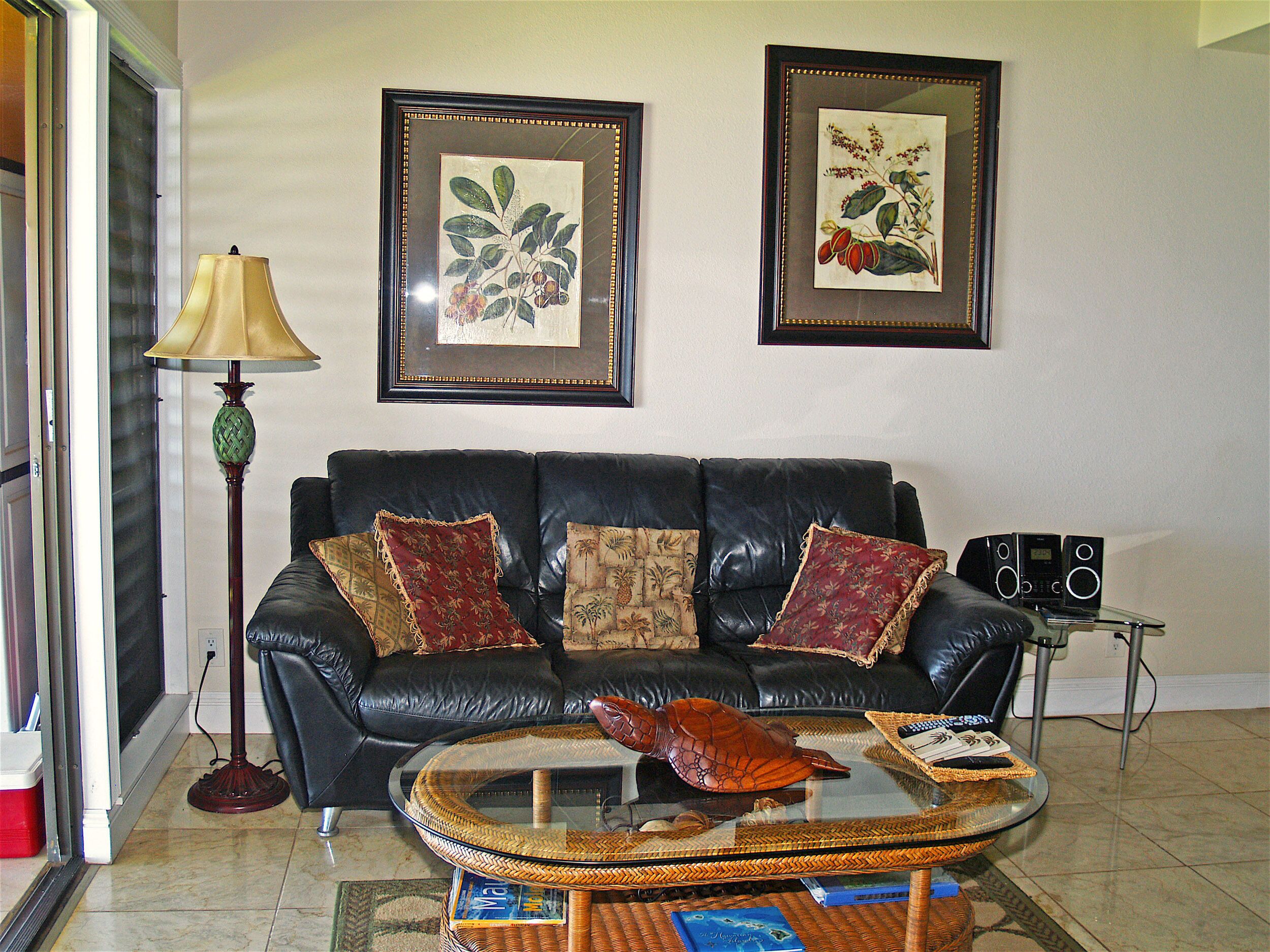 A living room with a black leather sofa, a glass coffee table, and framed botanical prints on the wall.