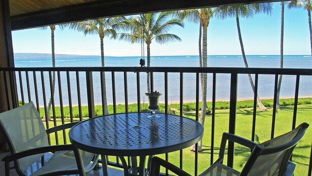 A balcony with a round table and four chairs, overlooking a beach with palm trees and the ocean.