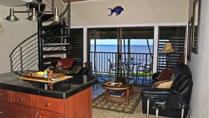 A spacious living area with a view of the sea, a dining area with outdoor seating, and a kitchen with a central island.