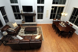 A living room with a fireplace, a sofa, a coffee table, and a dining table with chairs. - Beautiful 5 bedroom + sleeping loft ski-in/ski-out Mountain House (Granby)