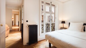 Hotelkamer met een groot bed, een radiator, een raam met uitzicht en een deur naar een andere kamer.
