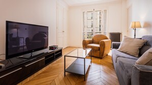 Een woonkamer met een flatscreen televisie, een glazen salontafel, een bank en een fauteuil.