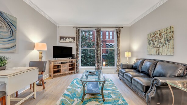 A modern living room with a glass coffee table, leather sofa, and a television on a wooden stand. - Romantic Condo in City Center- Wright Square Loft C (Savannah)