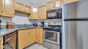 A kitchen with wooden cabinets, a stainless steel refrigerator, a microwave, and an oven. - Romantic Condo in City Center- Wright Square Loft C (Savannah)