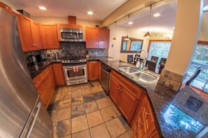 A modern kitchen with wooden cabinets, stainless steel appliances, a tiled backsplash, and a large window providing natural light. - Snowy Creek 4 - Ski in Ski out, Private Hot Tub, Short Walk to Whistler Village (Whistler)