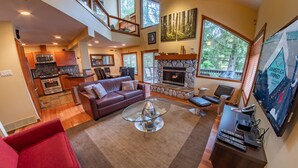 A spacious living area with a fireplace, a red sofa, and a dining area with a view of the outdoors. - Snowy Creek 4 - Ski in Ski out, Private Hot Tub, Short Walk to Whistler Village (Whistler)