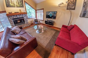 A living room with a stone fireplace, leather sofas, a red couch, and a TV on the wall. - Snowy Creek 4 - Ski in Ski out, Private Hot Tub, Short Walk to Whistler Village (Whistler)