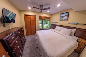 A bedroom with a bed, wooden dresser, ceiling fan, window with blinds, and artwork on the walls.