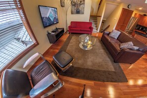 A modern living room with a red sofa, a glass coffee table, and a TV on the wall. - Snowy Creek 4 - Ski in Ski out, Private Hot Tub, Short Walk to Whistler Village (Whistler)