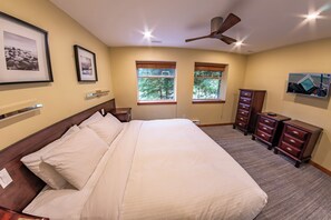 Un dormitorio con una cama grande, dos ventanas con persianas, un ventilador de techo y un aparador.